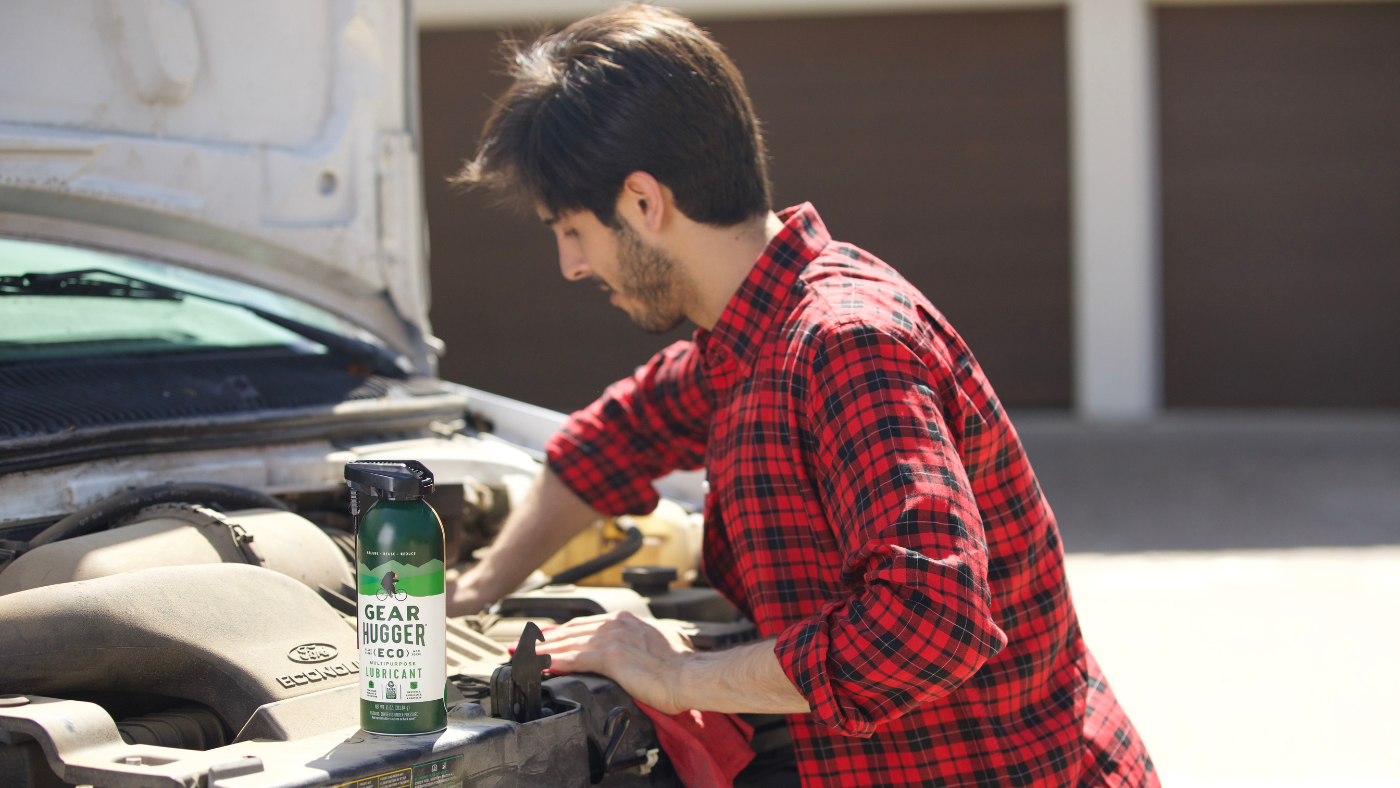 Man applying Gear Hugger eco-friendly lubricant spray to car engine in garage