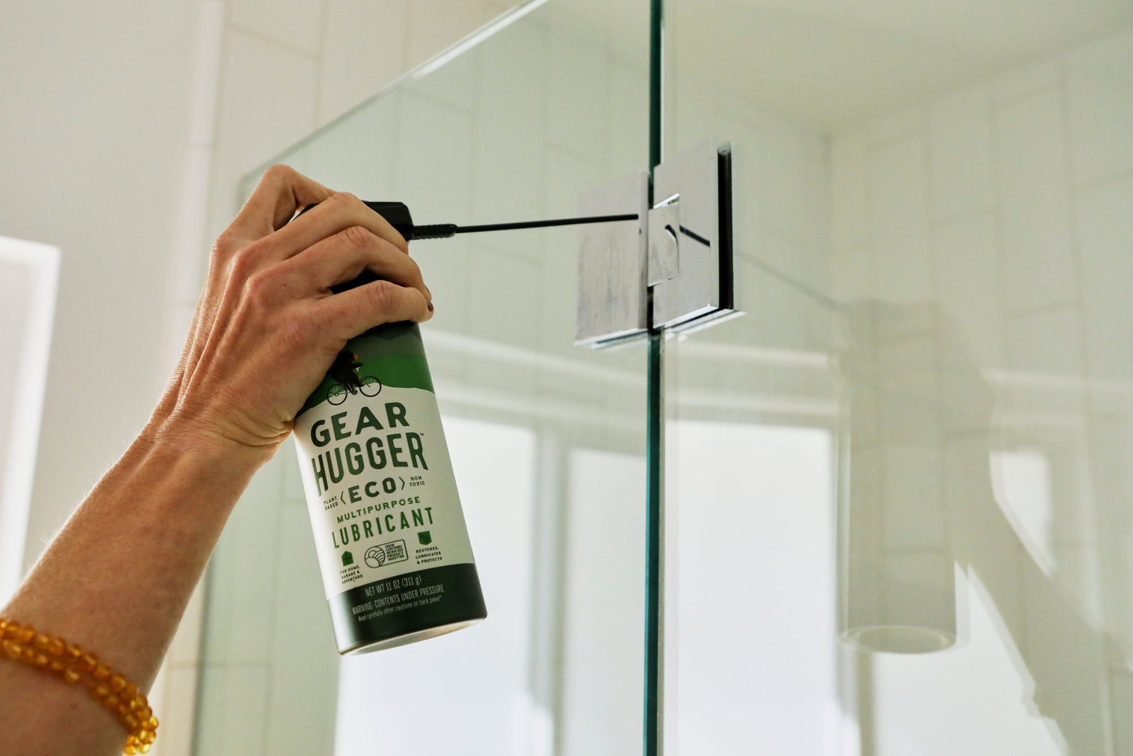 Applying Gear Hugger eco-friendly lubricant to a bathroom door hinge for a healthy home
