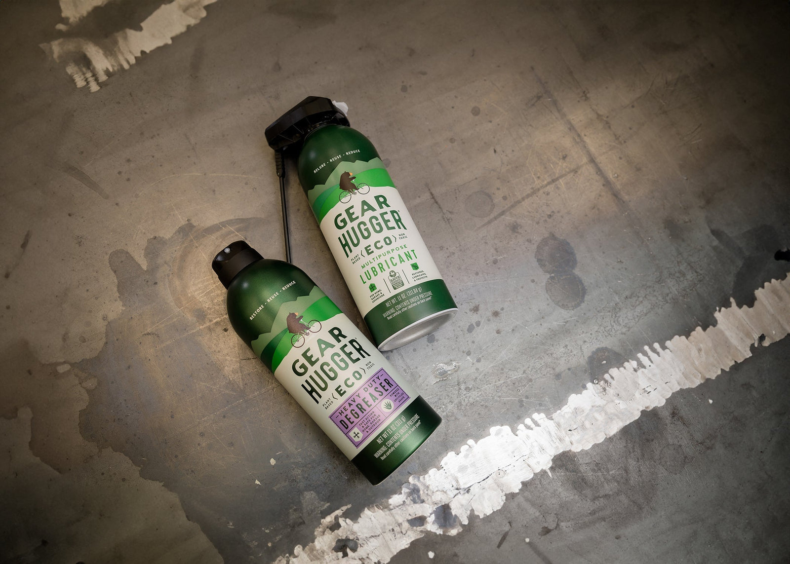 Two Gear Hugger eco-friendly spray lubricant and degreaser cans on concrete floor
