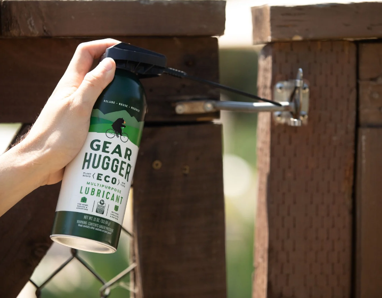 Eco-friendly plant-based lubricant spray being applied to a squeaky outdoor wooden gate hinge